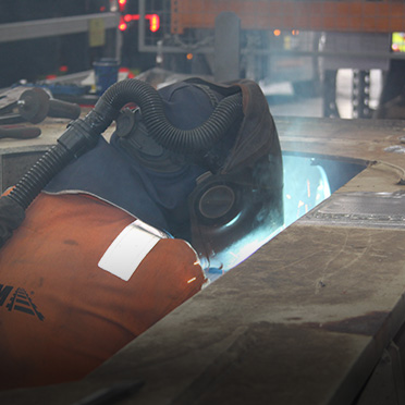 A man in an orange reflective jacket and a protective helmet works on welding.