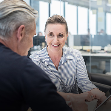 A man and woman talk to each other in an office space with computers.